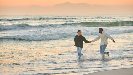 Casually Dressed Loving Young Couple Running Along Beach Shoreline Through Waves At Sunrise