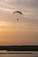 A paraglider or paramotor flying during a beautiful sunset over the beach. Real Photo