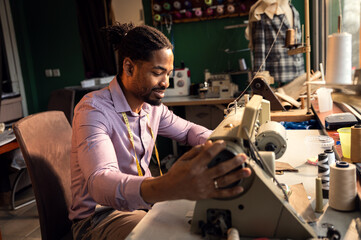 Male fashion tailor working on the sewing machine for the suit design in his workshop.