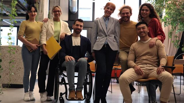 Diverse Team of Professionals Posing in Office Space - A dynamic group of six professionals, including one in a wheelchair, smiling in an office.