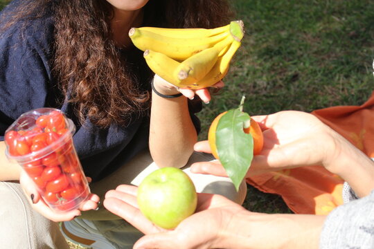 close-up of two friends out on a picnic in the garden holding healthy fresh fruits 