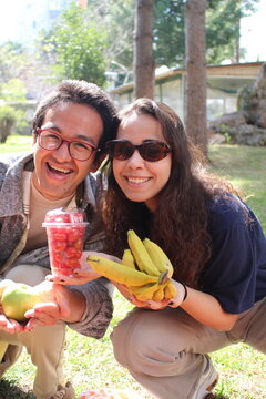 two friends out on a picnic in the garden smiling and holding healthy fresh fruits *4