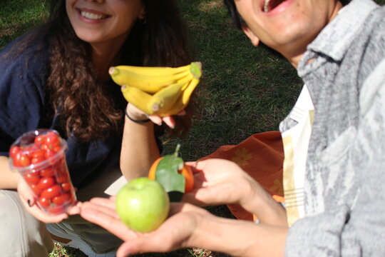 close-up of two friends out on a picnic in the garden smiling and holding healthy fresh fruits *6