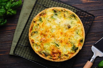 Unsweetened pastry, a whole quiche with spinach, oyster mushrooms, egg filling and cheese on a baking rack on a dark wooden background. Spinach recipes.