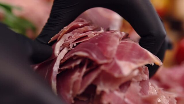 Close-up shot of prosciutto slices in hands of person with black gloves, traditional Italian antipasto and delicacy, dry-cured ham slices
