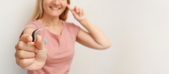 Happy woman enjoys a life and can hear surrounding sounds thanks to a hearing aid behind her ear. Lady with hearing aid put her hand to her ear against white background