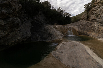 A secluded waterfall flows into a serene pond, surrounded by rocky terrain and lush greenery, evoking a sense of tranquility