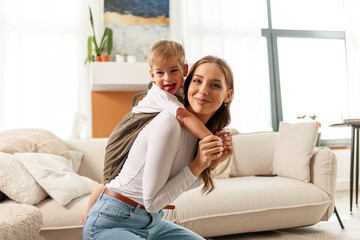 Obraz premium young mother holds her little son in her arms and lifts him up at home, a 2-year-old boy is having fun