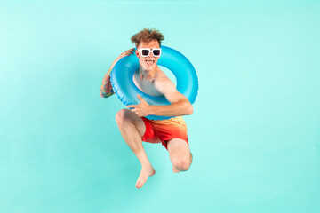 young cheerful guy winner with inflatable swimming ring jumps and flies on blue isolated background in summer