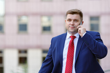 Portrait of handsome young businessman in suit with phone walking outdoors