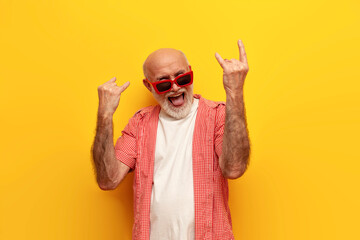 old grandfather pensioner in sunglasses shows rock gesture and sings to the music at party on...