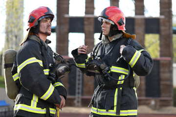 Two firefighters in equipment and red helmets on test area, lead discussion