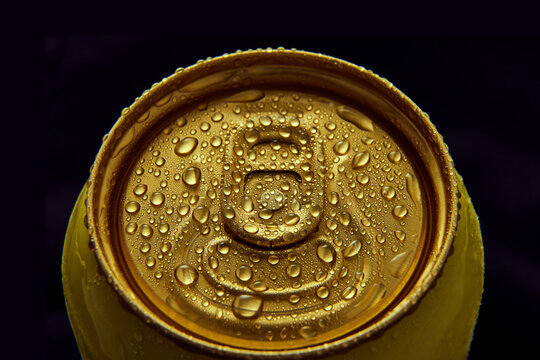 Close-up photo of golden aluminum closed can, jar of beer, coke, soda with condensation water drops on black background. Concept of alcohol and non-alcohol drinks, refreshment. Poster, banner for ad