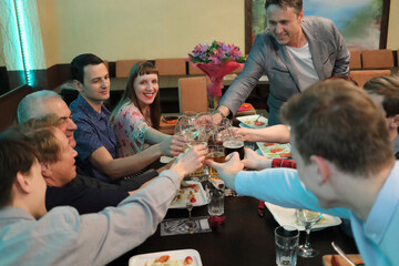 seven guests at table on anniversary, holding glasses and toasting, happy festive moment