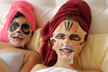 two girls with decals of animals on their faces, hair wrapped in towel, cropped