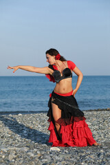 Dancer woman in black and red suit with fan dancing on seashore, gesture