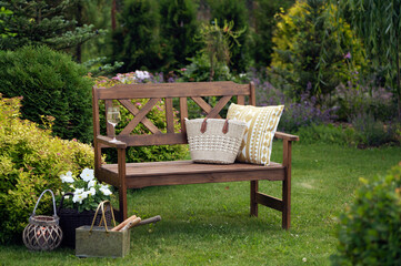 summertime relax in cottage garden. Wooden bench with pillow, lantern and petunia in flowerpot.