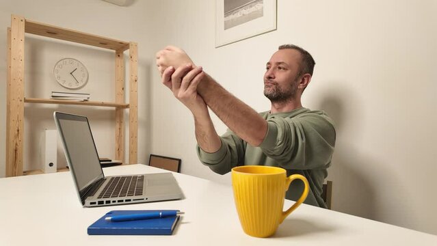 Man stretching painful hands and arms while working on a laptop.	
