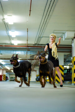 Running blonde with two pulling Doberman on leashes in the underground parking