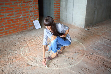 On the place of the future table woman draws chalk circle on the floor in newly built room