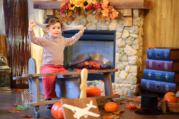 Portrait of happy little boy in the pilots cap on wooden plane in front of fireplace