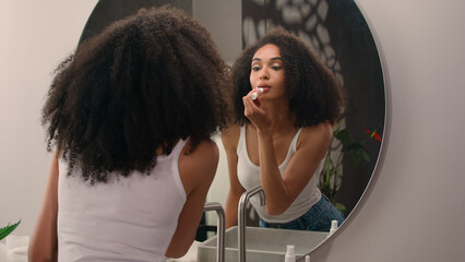 Young African American woman girl preparing morning beauty routine make-up cosmetic looking in...