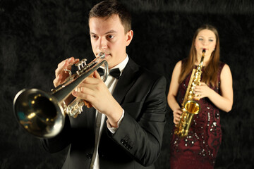 Man playing on trumpet in front of woman with saxophone in black room