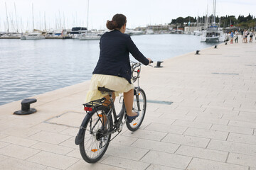 A woman in yellow dress and jacket is riding bicycle along the seafront