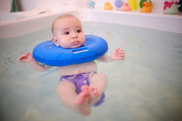 Fototapeta na wymiar A baby wearing a blue swimming cap is in a bathtub