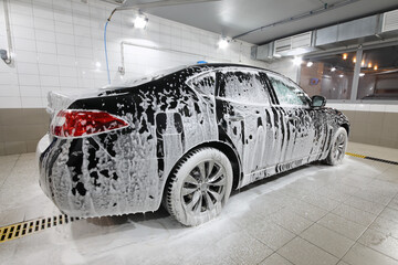 Black car covered with white foam during cleaning on car wash