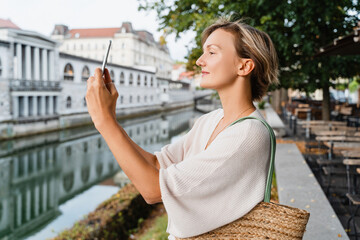 Smiling woman photographing cityscape architecture of Ljubljana old town, Slovenia. Travel Europe.