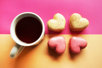 Heart-shaped macarons next to a cup of tea on a pink and yellow background