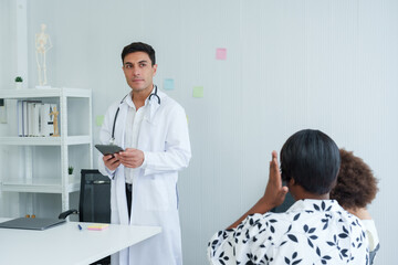 Obraz premium Medical professional in white coat holds tablet, attention focused on digital device, standing in clinic office with anatomical model behind..Physician with digital pad, engrossed in electronic data