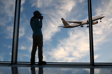 Silhouette of boy who takes photograph of take-off plane