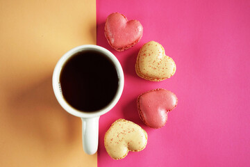 Heart-shaped macarons next to a cup of tea on a pink and yellow background