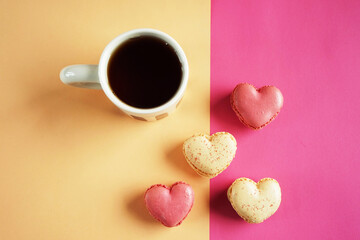 Heart-shaped macarons next to a cup of tea on a pink and yellow background