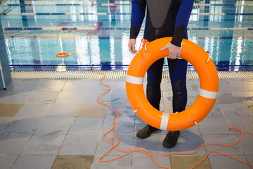 Instructor is holding lifebuoy near pool in training center.