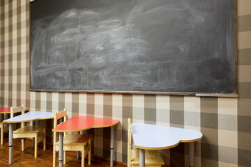 Blackboard on wall, desks with chairs in classroom at children club.