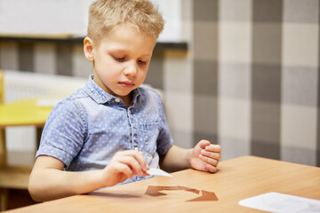 Little boy solves puzzle sitting at desk in room.
