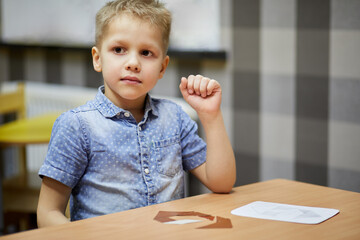 Little boy sits at desk with paper puzzle.