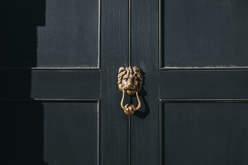 Close up of a lion's head door knocker on a black door.