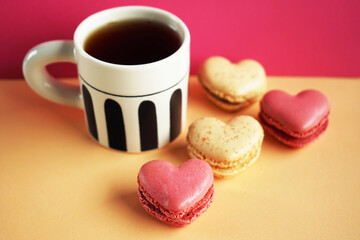 Heart-shaped macarons next to a cup of tea on a pink and yellow background