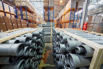 Packages of plastic pipes and cardboard boxes on shelves in factory warehouse. 