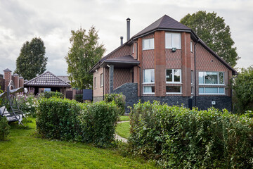 Modern cottage house of red brick and garden with flowers, bushes, trees.