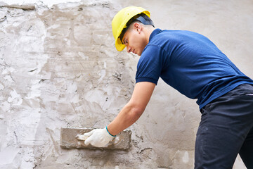Young male labor with trowel plastering on wall with concrete at construction site