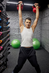 Man doing exercises with two kettlebells in gym.