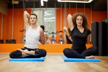Man and woman sit in lotus position on mats in gym.