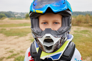 Portrait of boy in helmet for motorbike racing standing outdoor.