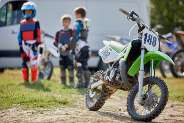 Sports motorbike and several boys in suits and helmets at background.