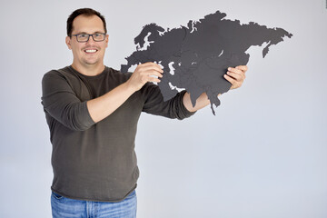 Smiling man in glasses holds puzzle map of Eurasia.